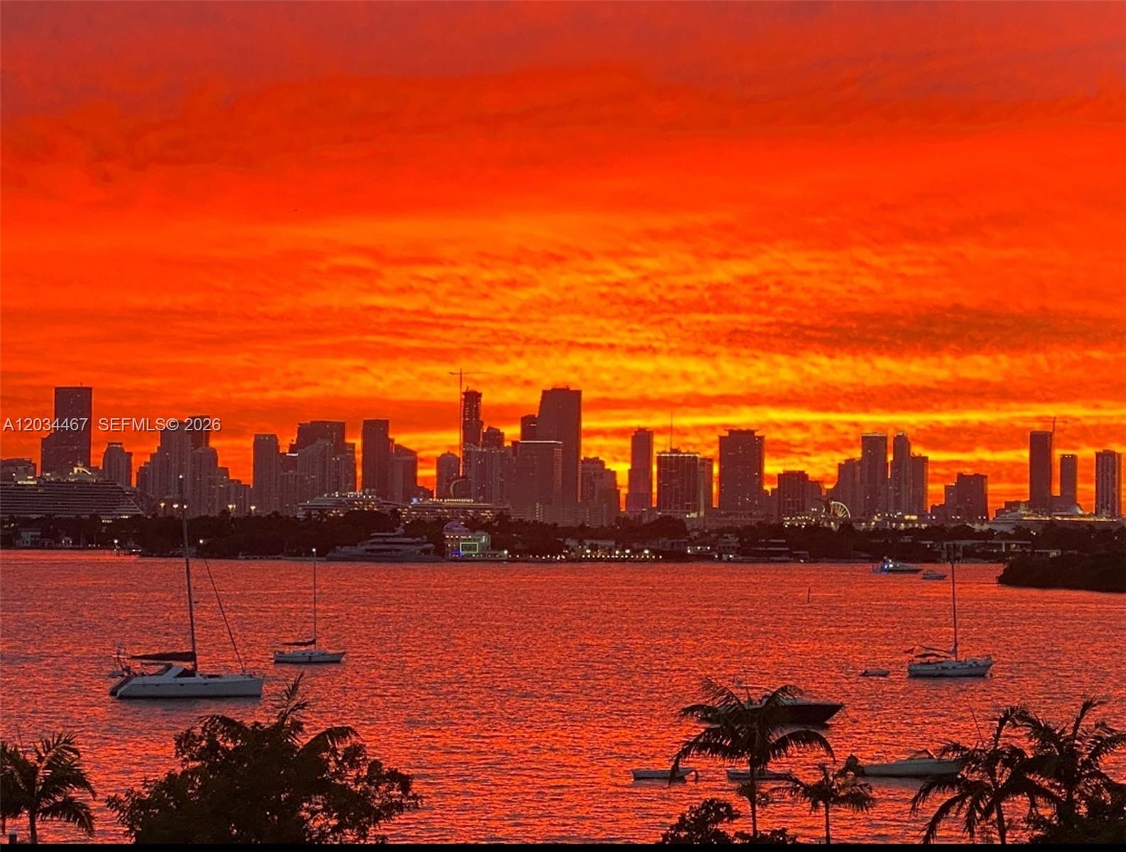 A vibrant sunset glows over the Miami skyline and a bay with several sailboats — MIAMI BEACH, FL