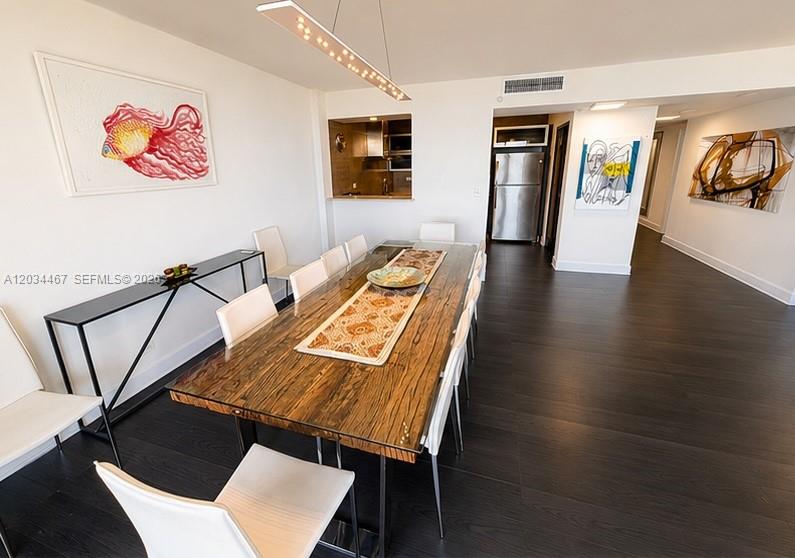 A dining room features a wooden table, white chairs, dark flooring, and modern wall art — MIAMI BEACH, FL