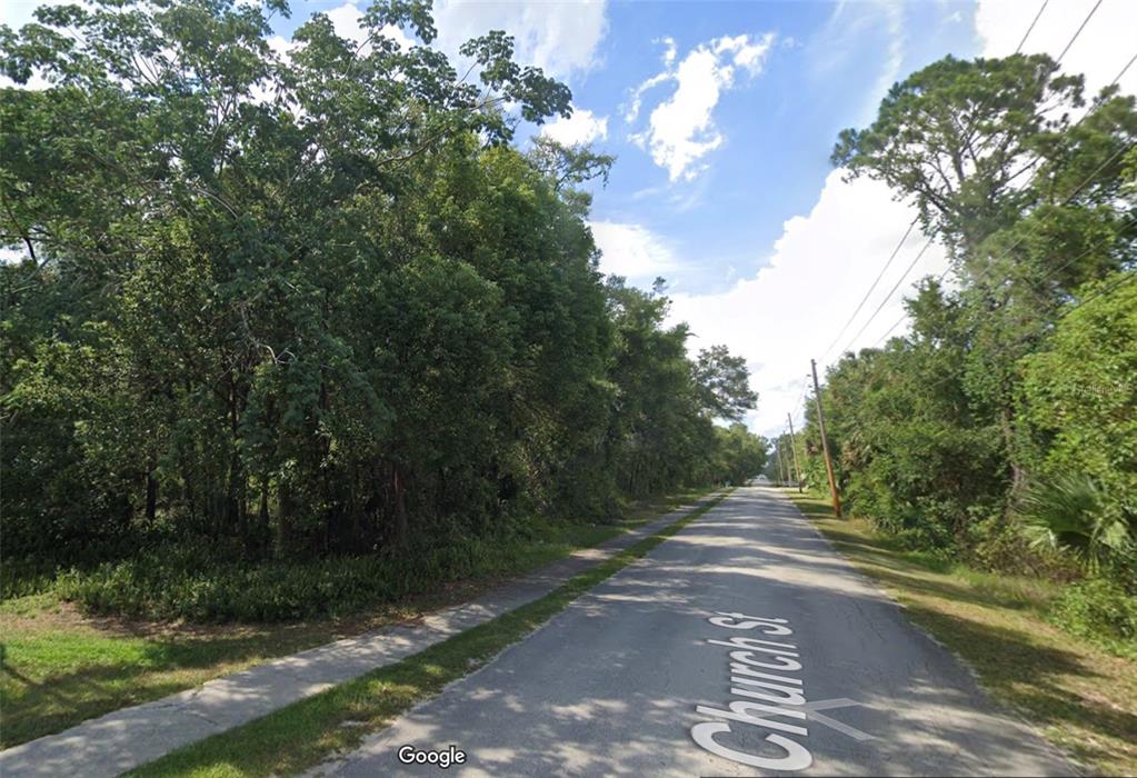 A paved road runs through a wooded area with a sidewalk on the left — CHURCH, LAKE HELEN, FL