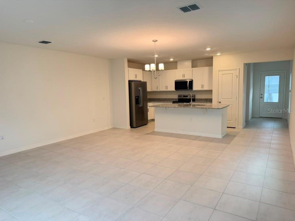 An open-concept kitchen with white cabinets, stainless steel appliances, and a granite-topped island — 16615 LUMINARY LOOP, CLERMONT, FL