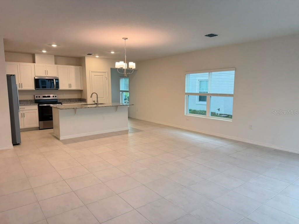 An open-concept kitchen with white cabinets and a breakfast bar overlooks a tiled living area — 16615 LUMINARY LOOP, CLERMONT, FL