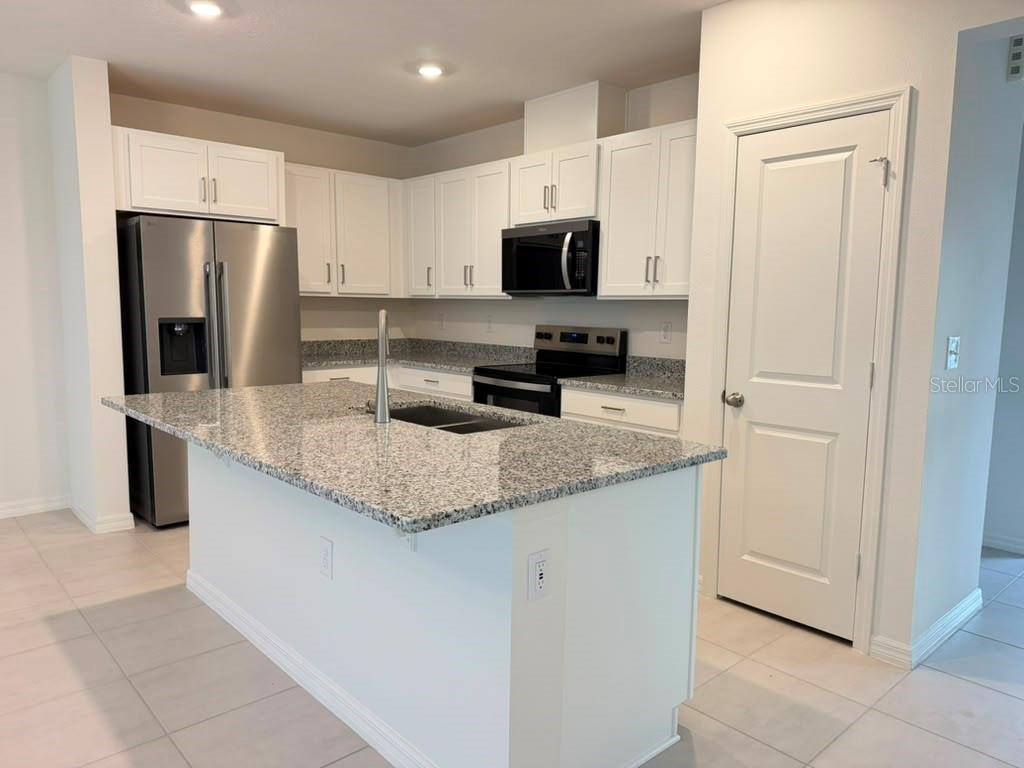 A kitchen with white cabinets, granite countertops, a center island, and stainless steel appliances — 16615 LUMINARY LOOP, CLERMONT, FL
