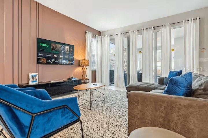 A living room features a blue velvet chair, a brown sofa, and a wall-mounted television — 1820 SANDY PARK TRAIL, KISSIMMEE, FL