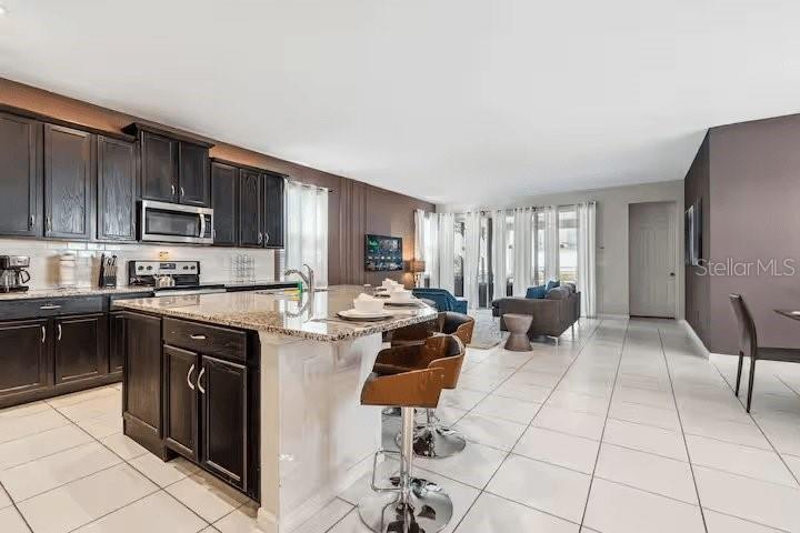 A kitchen with dark wood cabinets and a granite island overlooks an open living area — 1820 SANDY PARK TRAIL, KISSIMMEE, FL