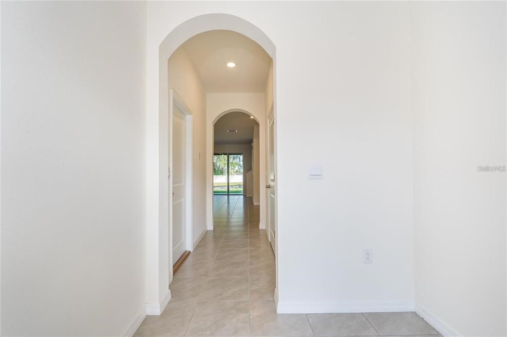 A hallway with tiled floors features two arched openings leading toward a rear sliding door — 34293 SORREL MINT DRIVE, WESLEY CHAPEL, FL