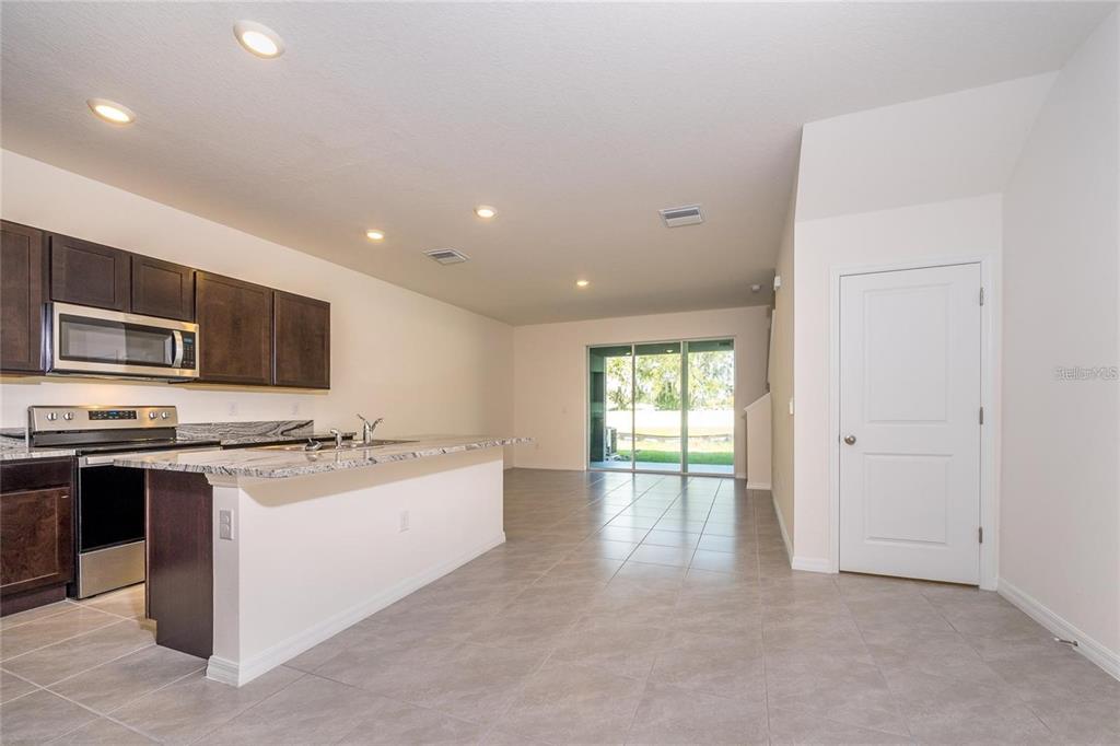 A kitchen with dark cabinets and granite countertops opens to a tiled living area — 34293 SORREL MINT DRIVE, WESLEY CHAPEL, FL