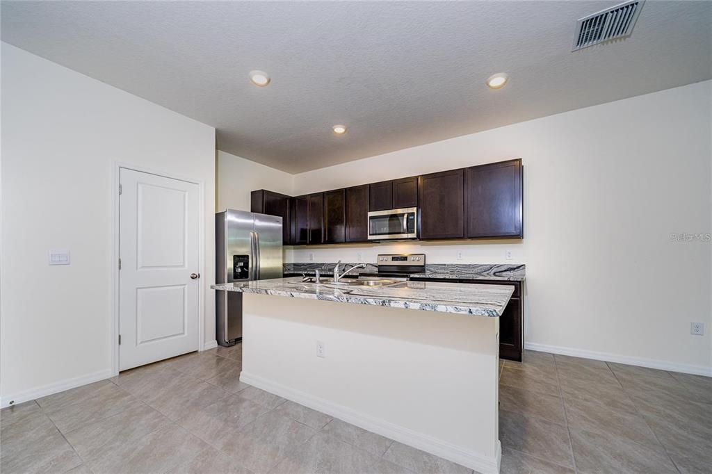 A kitchen features dark wood cabinets, granite countertops, stainless steel appliances, and tile flooring — 34293 SORREL MINT DRIVE, WESLEY CHAPEL, FL