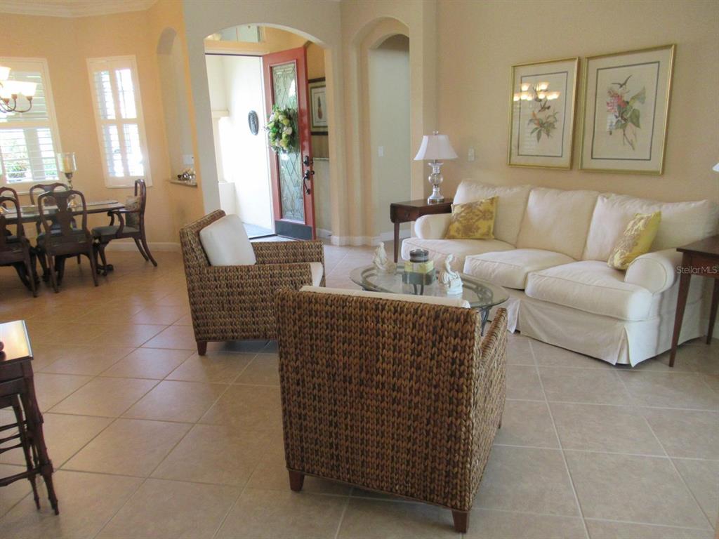 A living room with tile floors, a white sofa, two wicker chairs, and a dining area — 114 RIMINI WAY, NORTH VENICE, FL