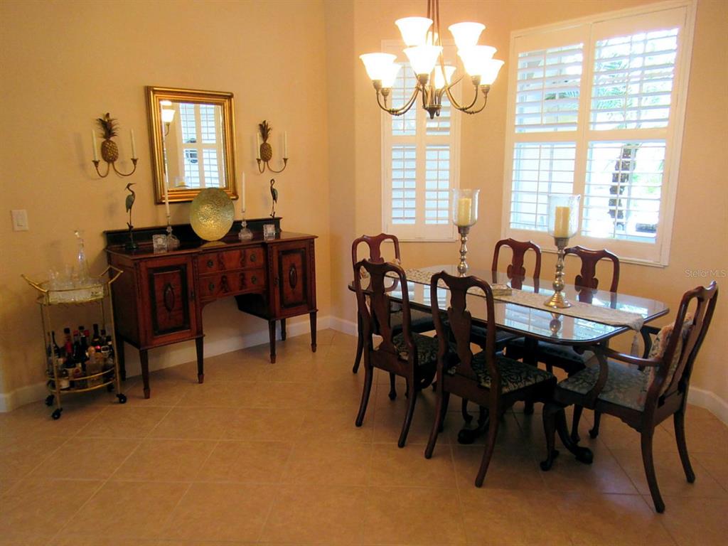 A formal dining room features a glass-topped table, dark wood chairs, and a matching sideboard — 114 RIMINI WAY, NORTH VENICE, FL