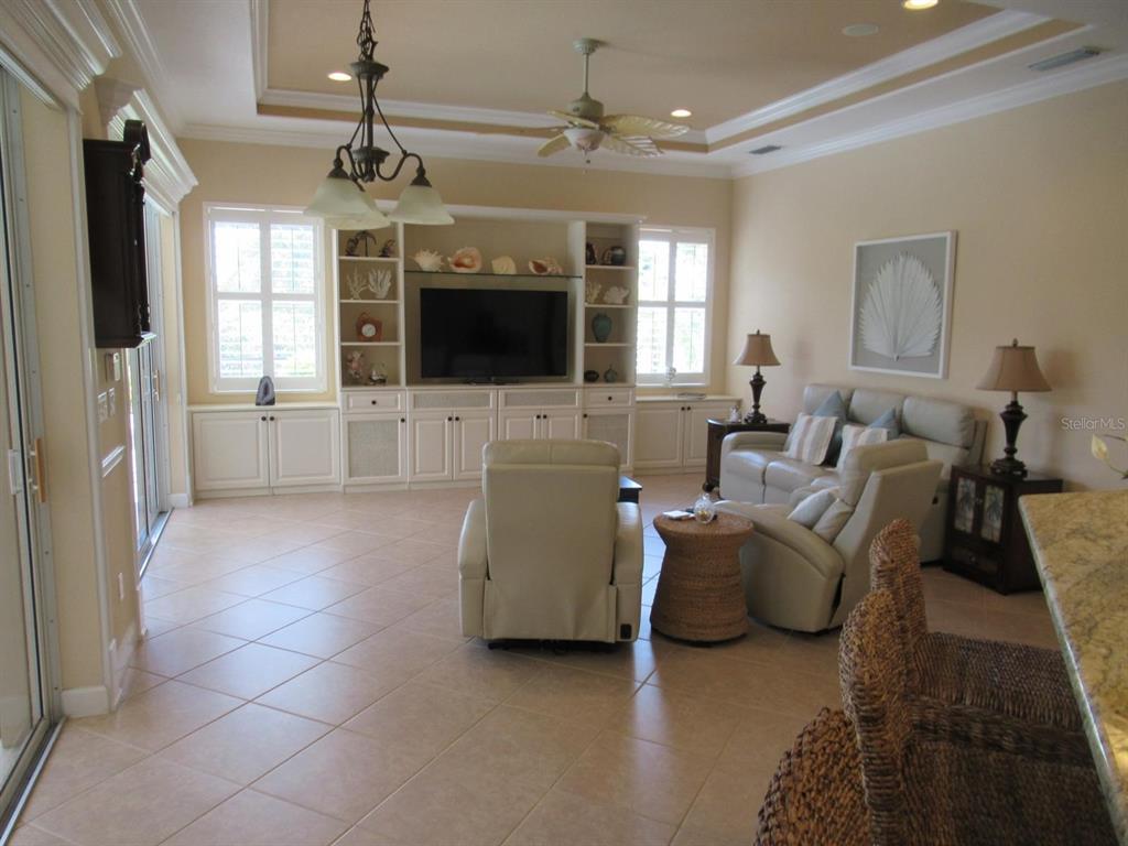 A living room features a built-in entertainment center, tile flooring, and a ceiling fan — 114 RIMINI WAY, NORTH VENICE, FL