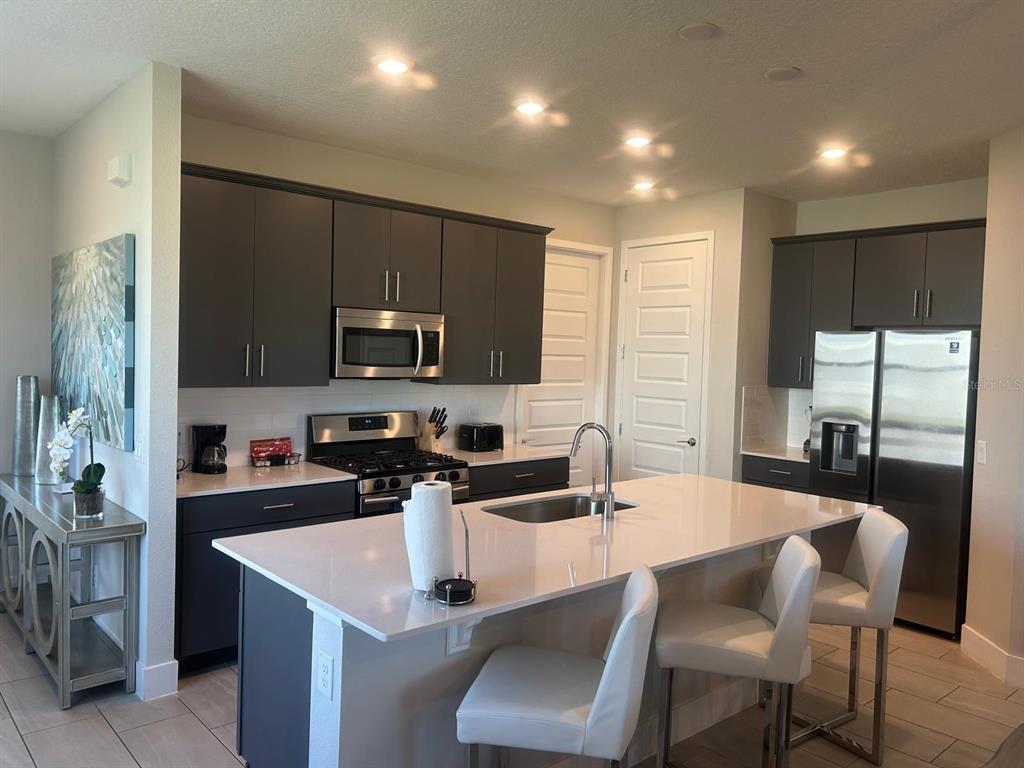 A modern kitchen features dark gray cabinetry, stainless steel appliances, and a large white island — 824 DRIVING RANGE COURT, REUNION, FL