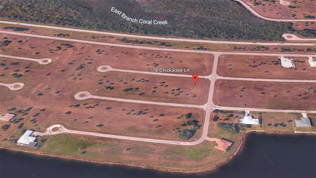 This aerial view shows a vacant residential lot in a suburban neighborhood near a creek — 18 CHICKADEE LANE, PLACIDA, FL