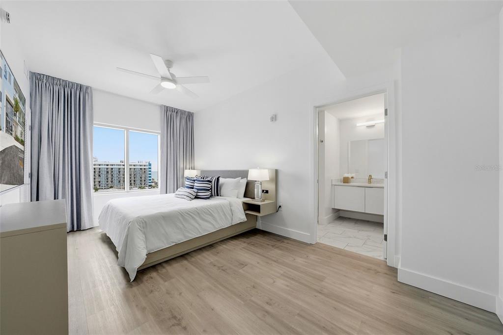 A modern bedroom features light wood flooring, a queen bed, and an attached bathroom — 411 E SHORE DRIVE UNIT 205, CLEARWATER BEACH, FL