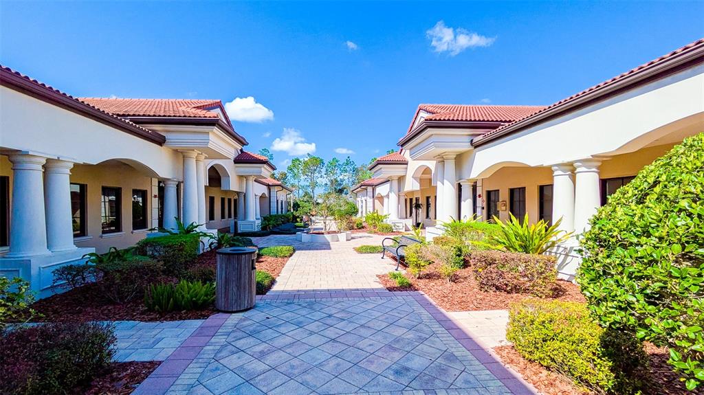 A paved courtyard sits between two symmetrical, single-story buildings with white columns and tiled roofs — 8946 77TH TERRACE E, LAKEWOOD RANCH, FL