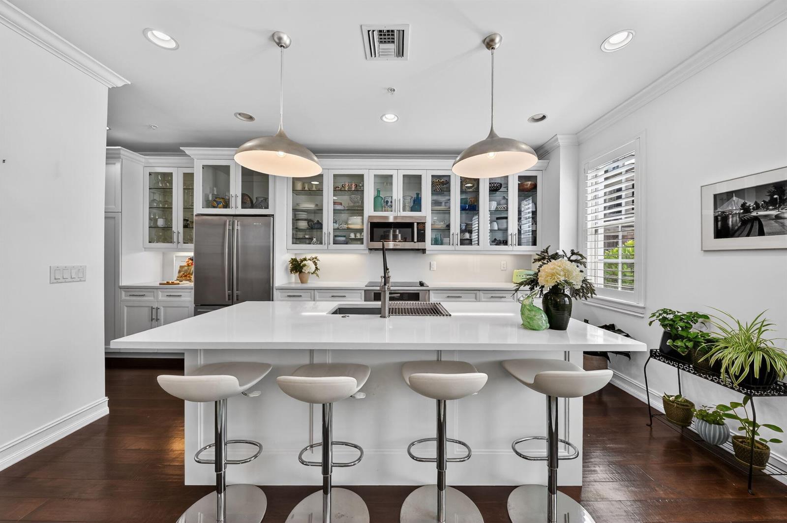 A modern white kitchen features a large island with four bar stools and pendant lighting — 145 N Cannery Row Circle, Delray Beach FL 33444, DELRAY BEACH, FL