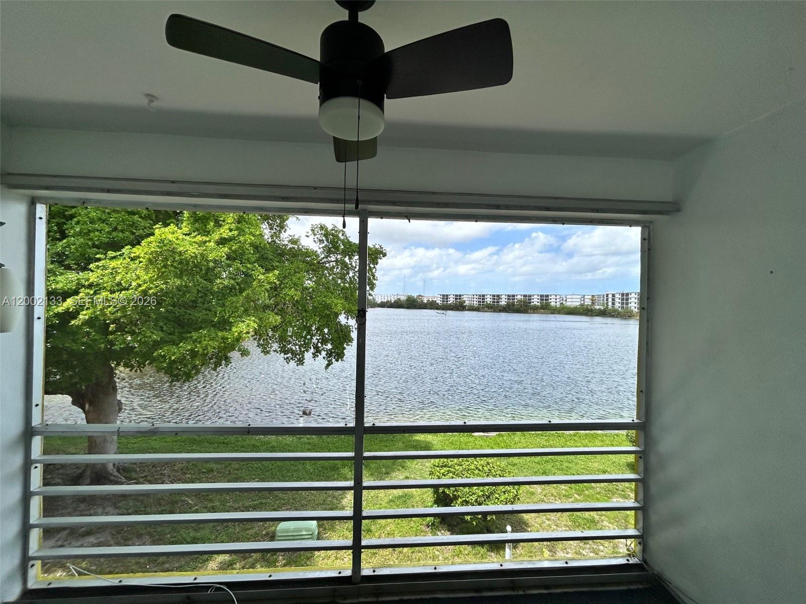 A screened-in porch features a ceiling fan and a view of a lake and trees — 245 NE 191st St # 3017, Miami FL 33179, MIAMI, FL