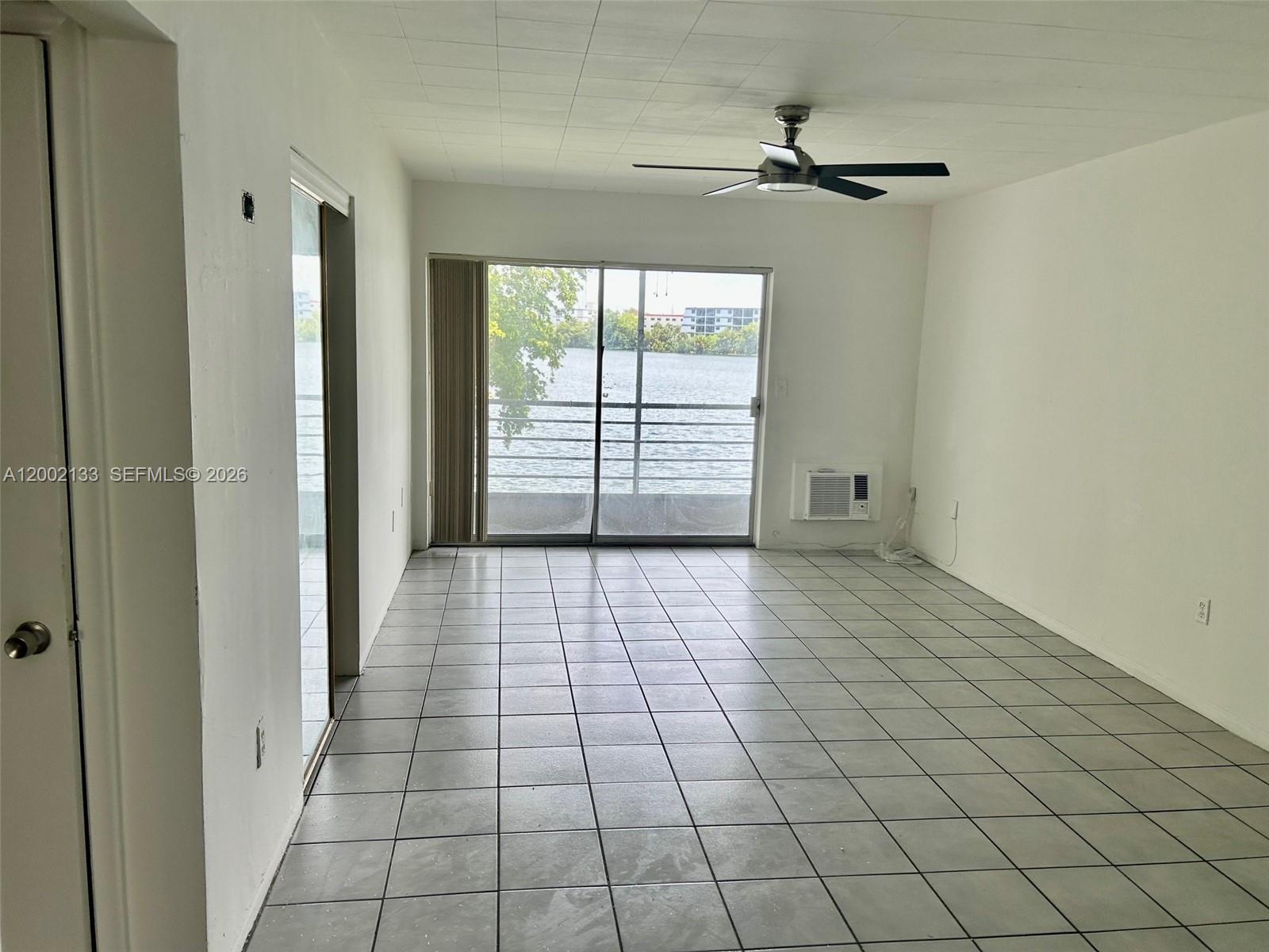 An empty room with gray tile flooring, a ceiling fan, and a sliding glass door — 245 NE 191st St # 3017, Miami FL 33179, MIAMI, FL