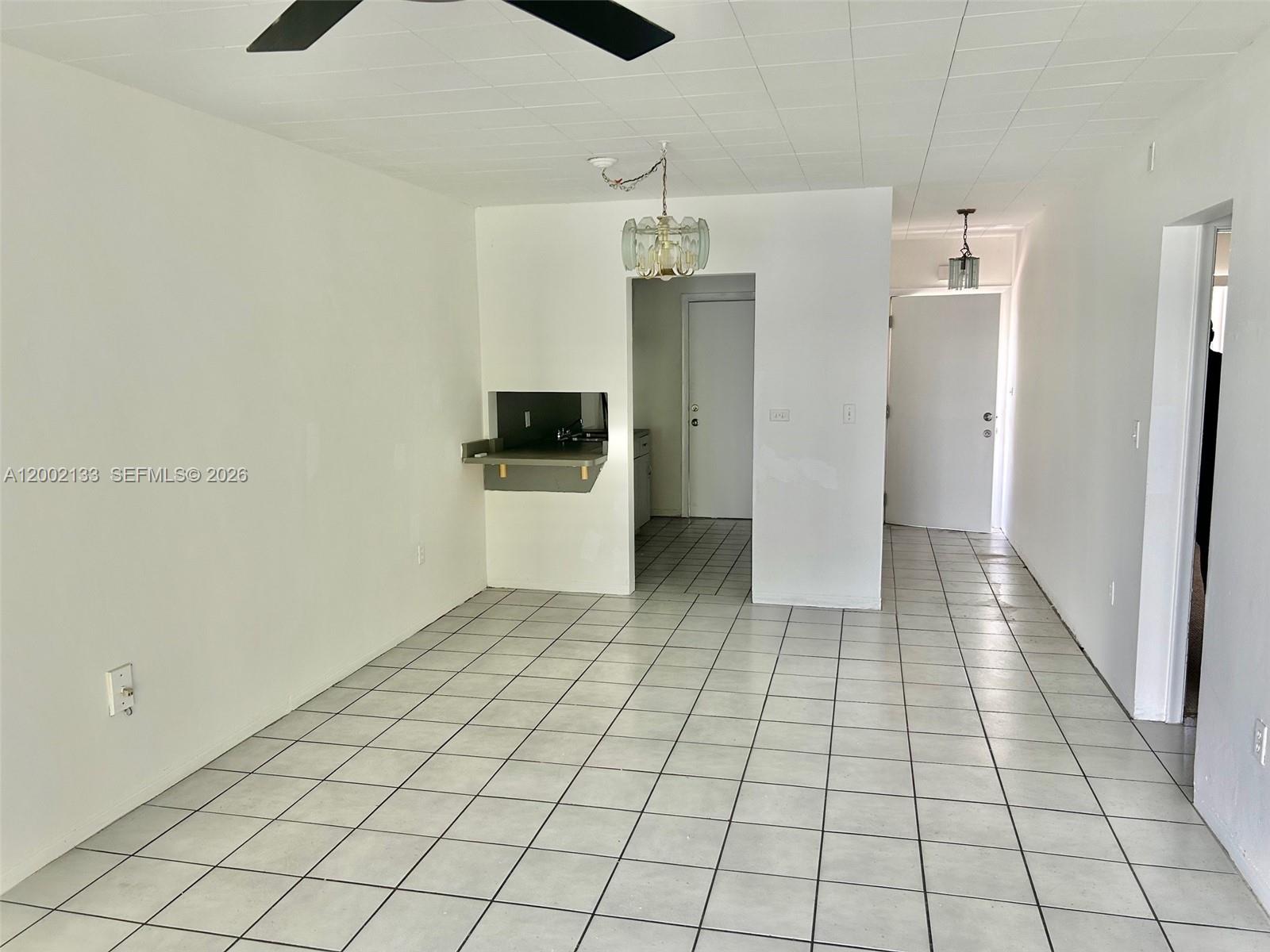 A room with white walls, tiled floors, a ceiling fan, and a small kitchen pass-through — 245 NE 191st St # 3017, Miami FL 33179, MIAMI, FL