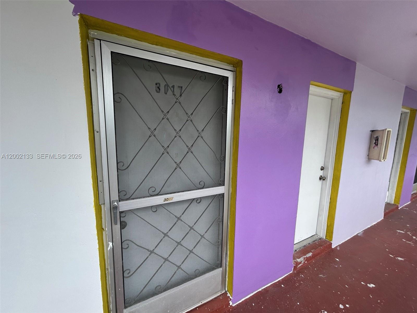A purple exterior wall features two doors with yellow trim and a metal security screen — 245 NE 191st St # 3017, Miami FL 33179, MIAMI, FL