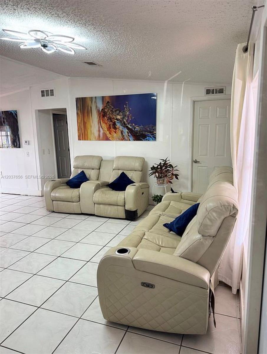 A living room features light-colored tile flooring, two beige reclining sofas, and a large abstract painting — 1133 SW 130th Ave, Miami FL 33184, MIAMI, FL