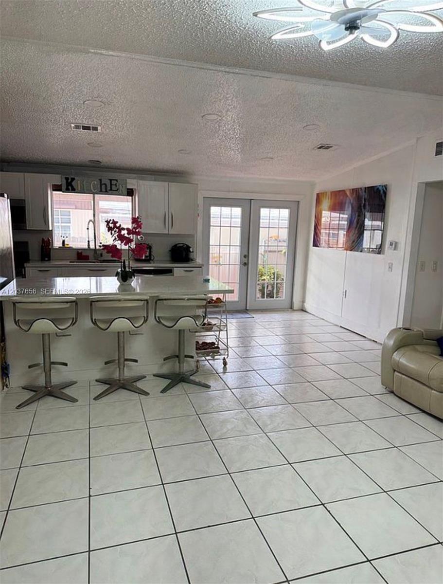 A kitchen with a white island, bar stools, and tile flooring opens to a patio door — 1133 SW 130th Ave, Miami FL 33184, MIAMI, FL