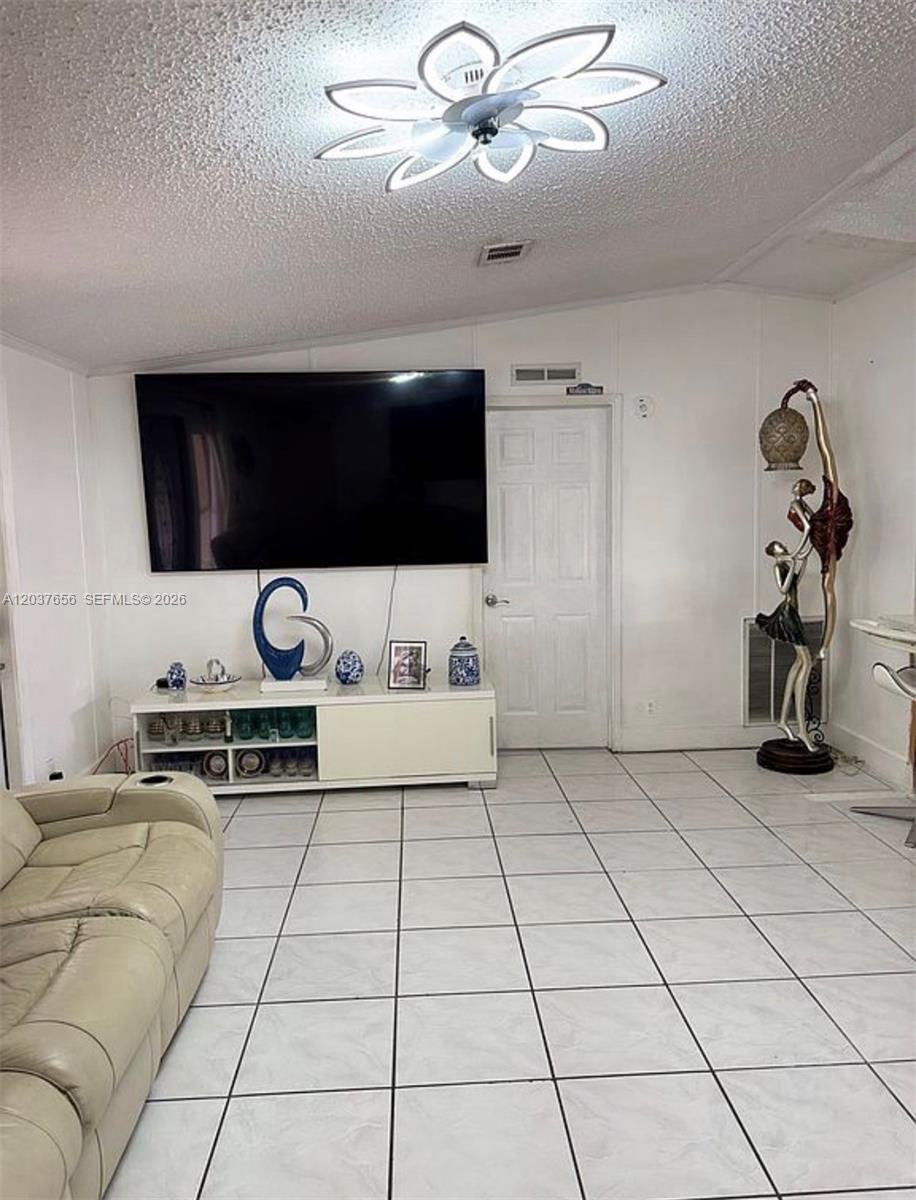 A living room features a large wall-mounted television, a white media console, and tile flooring — 1133 SW 130th Ave, Miami FL 33184, MIAMI, FL