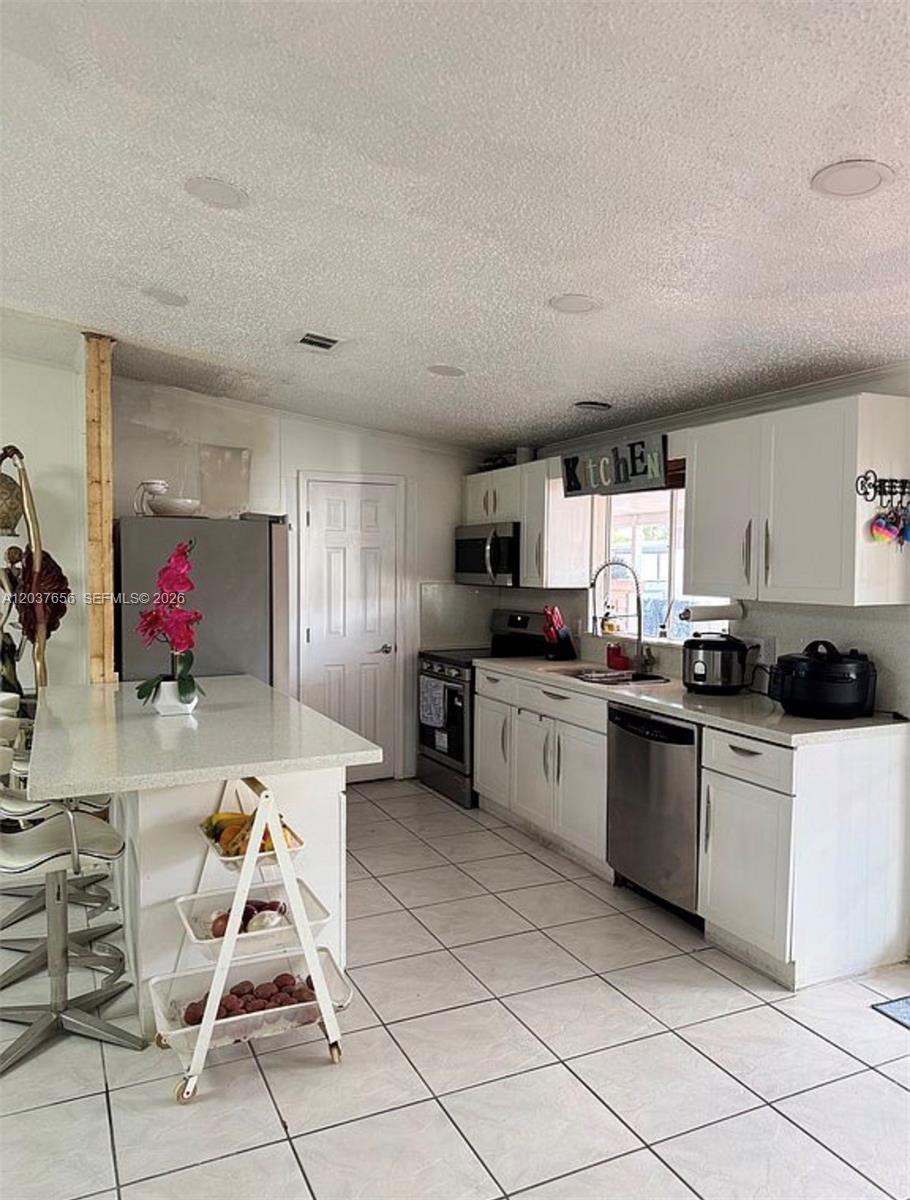 A kitchen features white cabinets, stainless steel appliances, a center island, and tiled flooring — 1133 SW 130th Ave, Miami FL 33184, MIAMI, FL