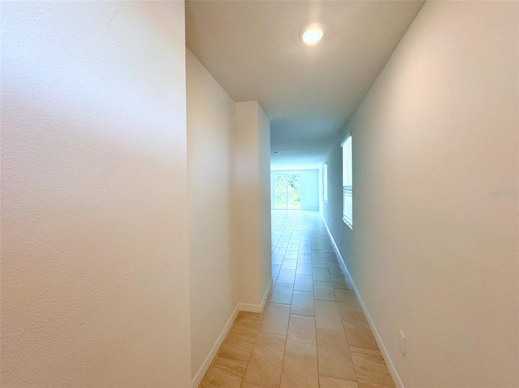 A long, narrow hallway with light-colored tile flooring leads toward a bright, open living area — 1461 BREKEY WAY, ZEPHYRHILLS, FL