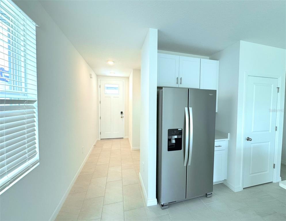 A stainless steel refrigerator stands in a kitchen area next to a tiled entryway hallway — 1461 BREKEY WAY, ZEPHYRHILLS, FL