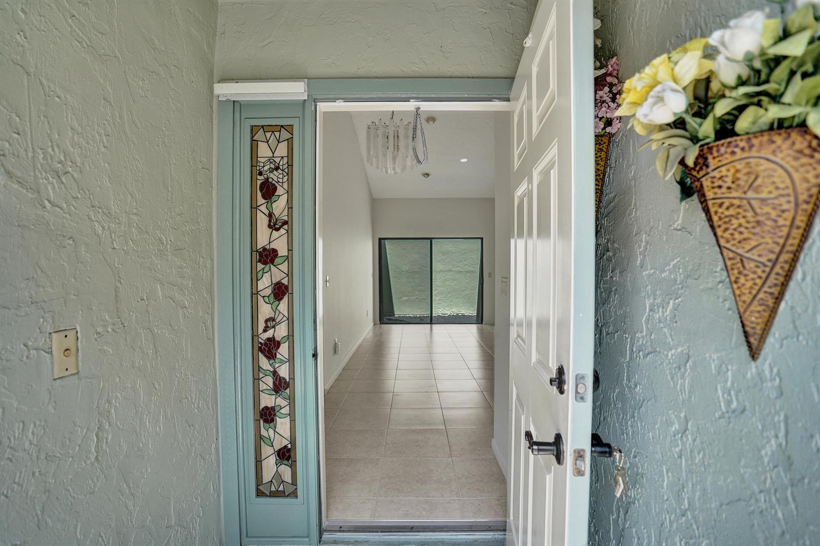 An open front door reveals a tiled entryway leading to a room with sliding glass doors — 2395 NW 15th Street, Delray Beach FL 33445, DELRAY BEACH, FL