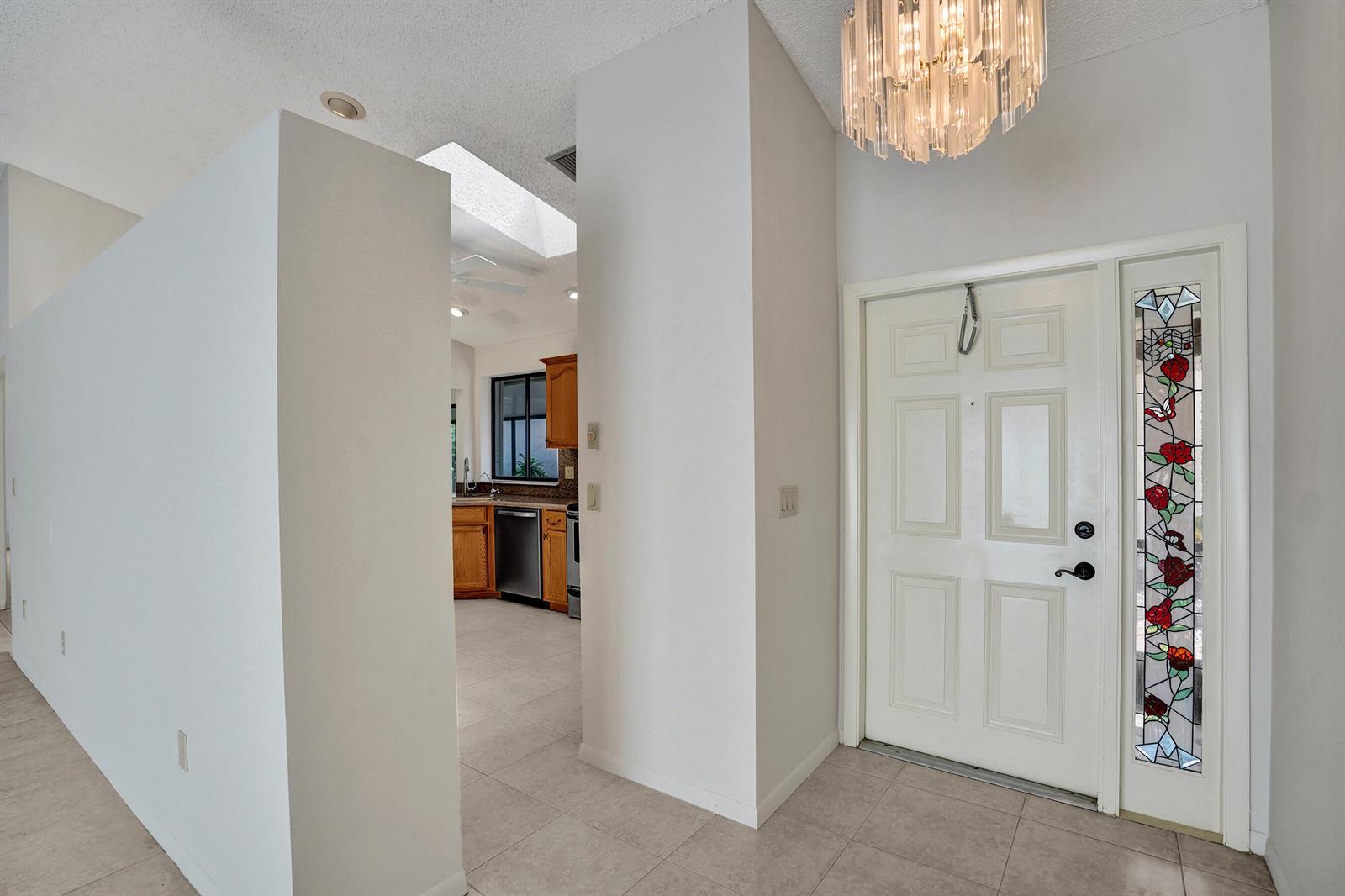 An entryway with a chandelier and stained glass door leads to a kitchen with cabinets — 2395 NW 15th Street, Delray Beach FL 33445, DELRAY BEACH, FL