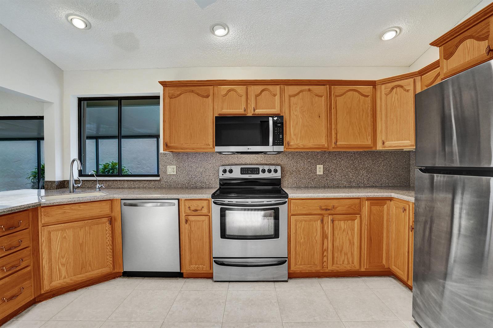 A kitchen features oak cabinets, stainless steel appliances, granite countertops, and light-colored tile flooring — 2395 NW 15th Street, Delray Beach FL 33445, DELRAY BEACH, FL