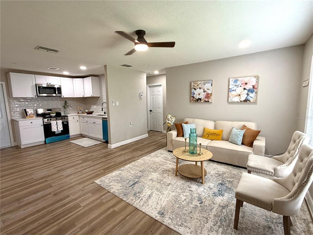 An open-concept living room and kitchen featuring white cabinets, wood-look flooring, and a beige sofa — 6612 SIERRA TERRACE, NEW PORT RICHEY, FL