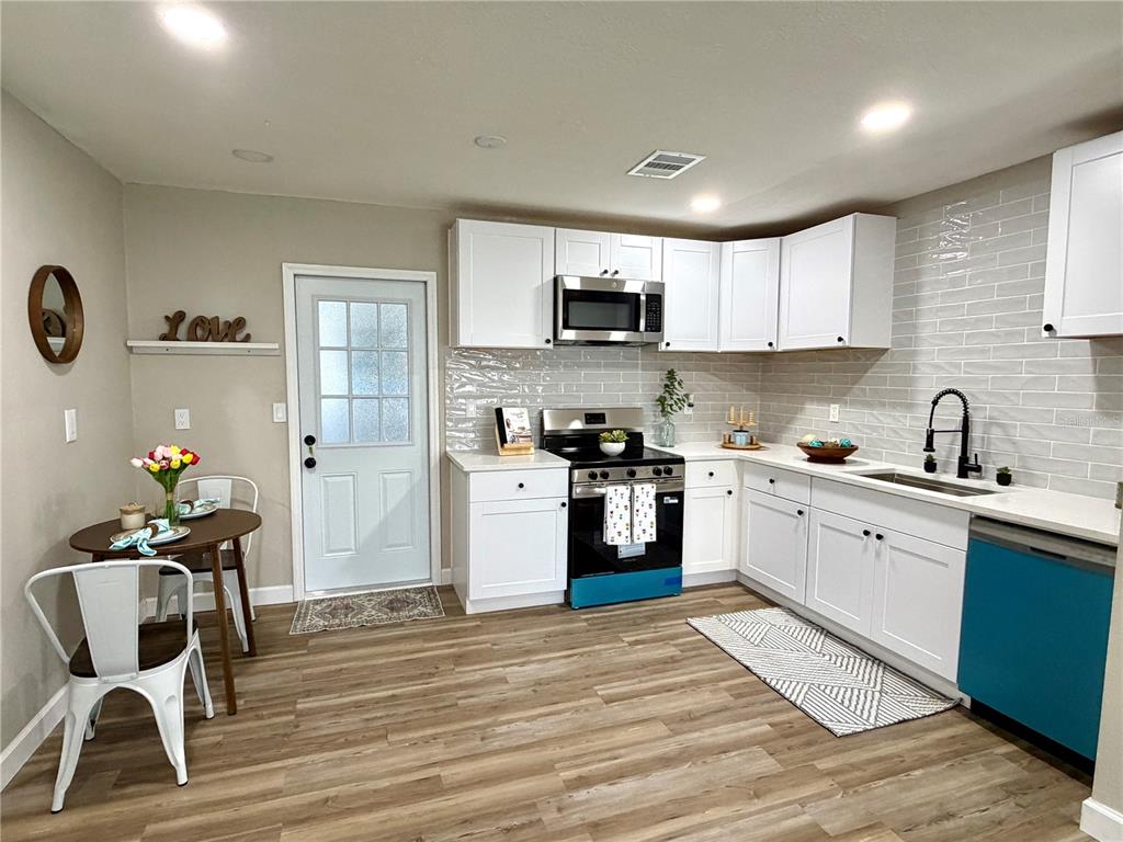 A kitchen features white cabinets, a subway tile backsplash, stainless steel appliances, and a dining area — 6612 SIERRA TERRACE, NEW PORT RICHEY, FL