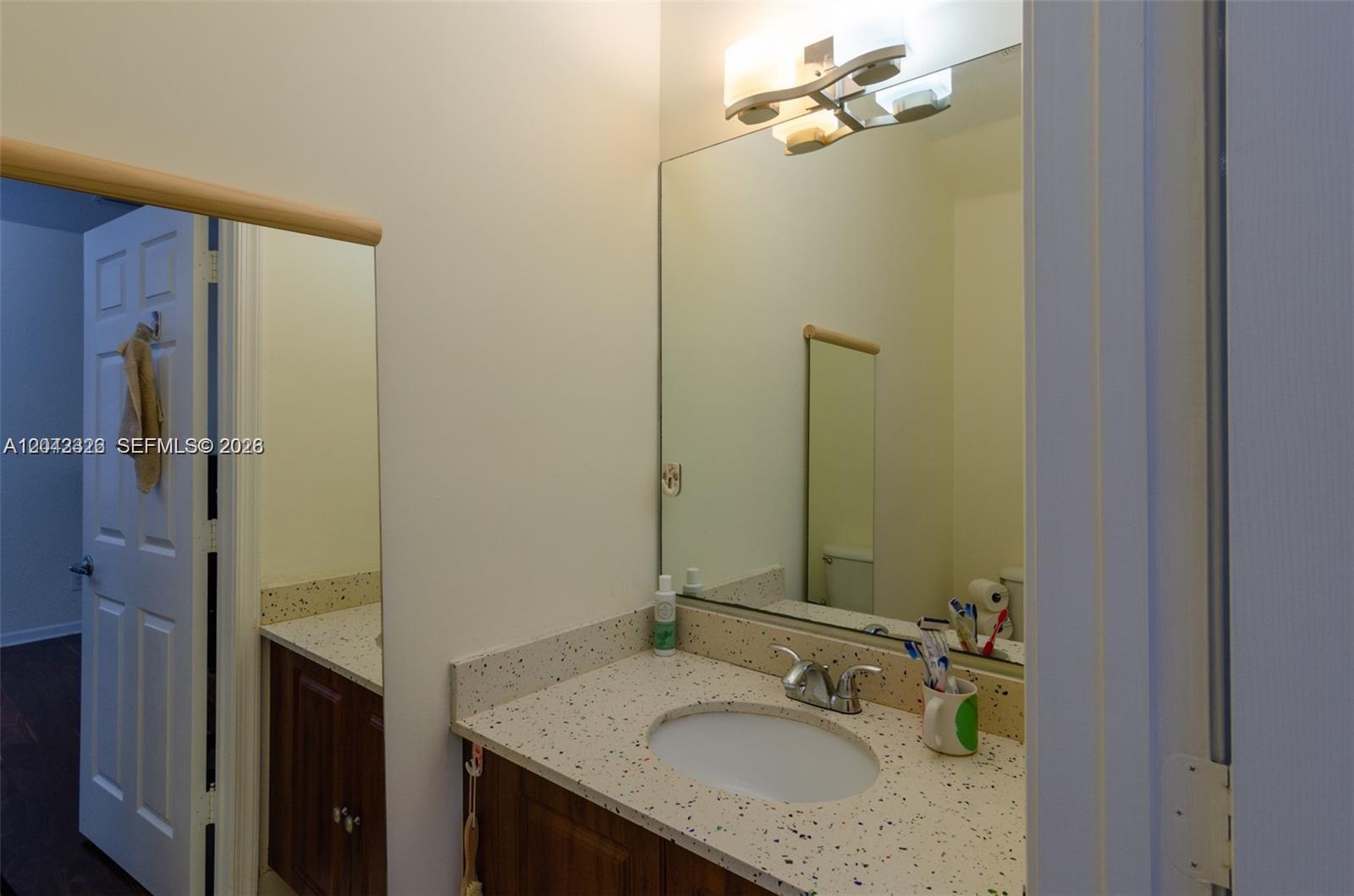 A bathroom features a speckled countertop, a wood vanity, and a large wall-mounted mirror — 4309 Vineyard Cir # 4309, Weston FL 33332, WESTON, FL