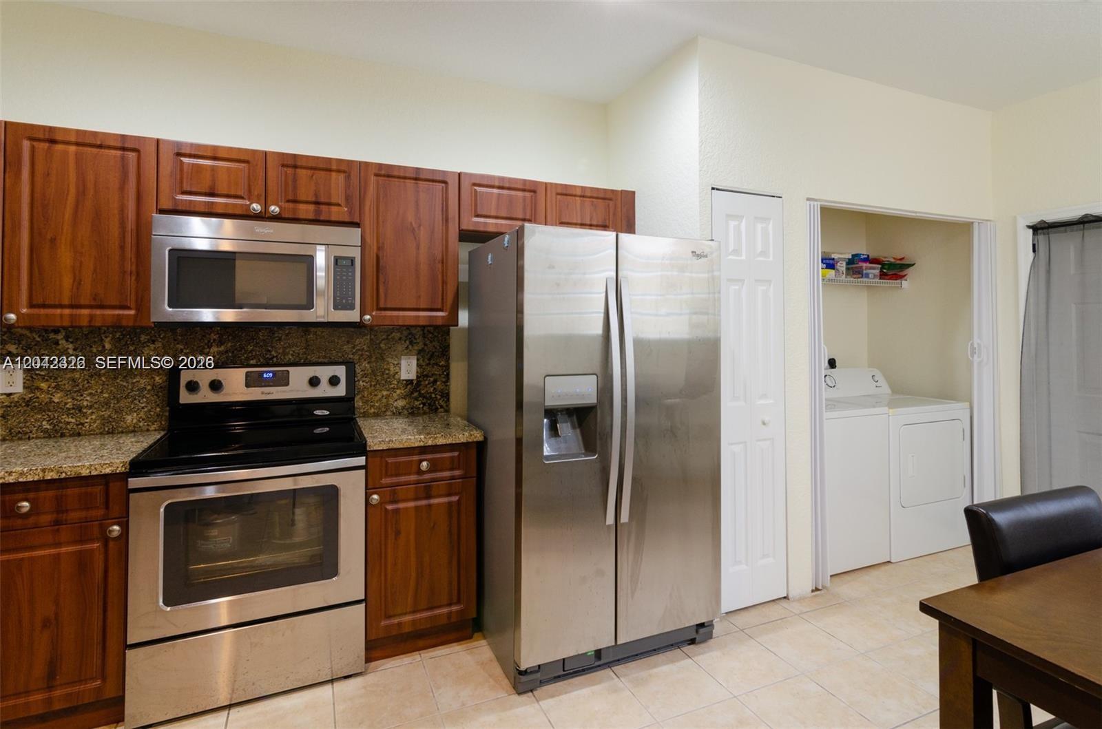 A kitchen features wood cabinets, stainless steel appliances, granite countertops, and an adjacent laundry closet — 4309 Vineyard Cir # 4309, Weston FL 33332, WESTON, FL