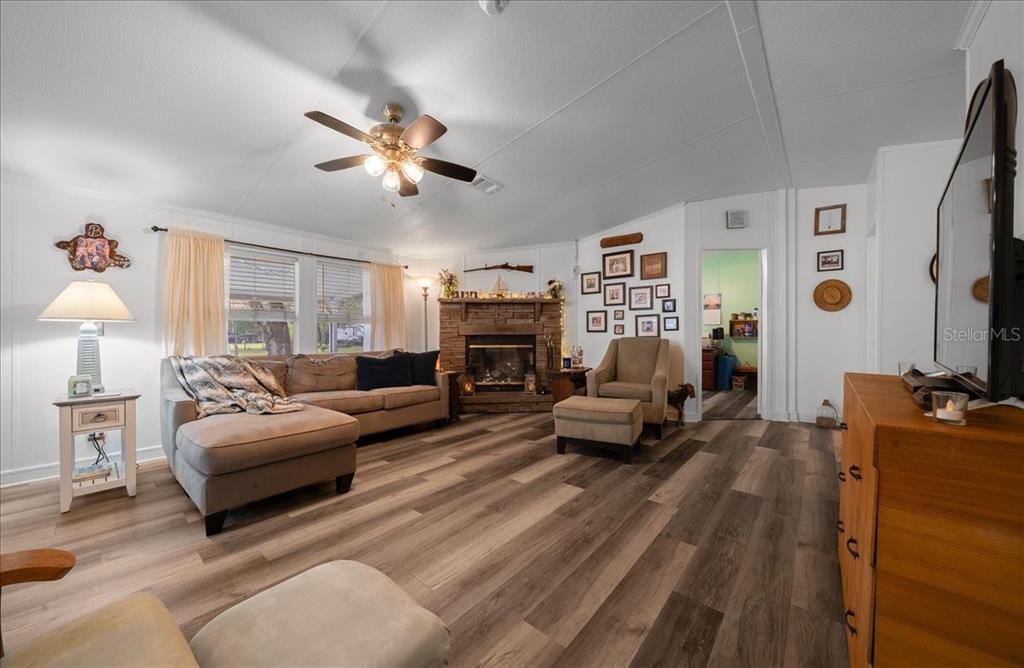 A living room features a stone fireplace, wood-look flooring, a ceiling fan, and a sectional sofa — 15701 NE 150TH AVENUE, FORT MC COY, FL