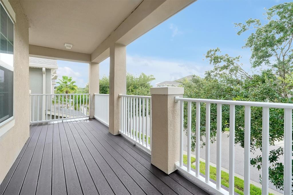 A covered balcony features dark wood-look decking and white railings overlooking trees and a street — 14699 MAGNOLIA RIDGE LOOP, WINTER GARDEN, FL