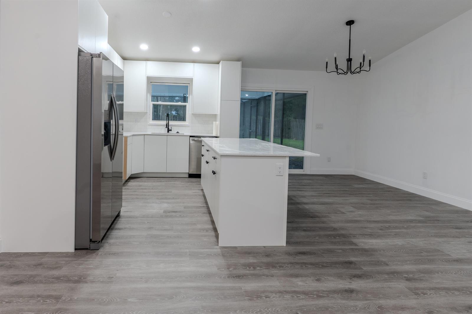 A modern kitchen features white cabinets, a marble-topped island, and gray wood-look flooring — 150 23rd Avenue, Vero Beach FL 32962, VERO BEACH, FL