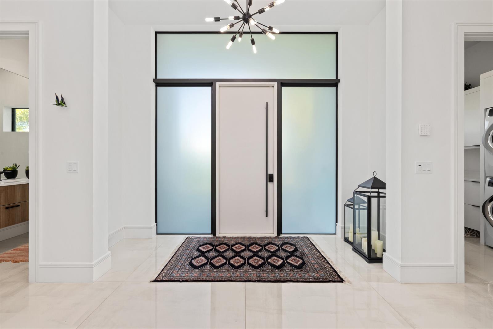 A modern entryway features a white door with frosted glass panels, a rug, and chandelier — 10 Coconut Road, Delray Beach FL 33444, DELRAY BEACH, FL
