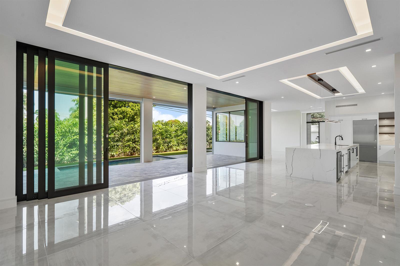 A modern open-concept living area with marble floors, a kitchen island, and large sliding doors — 10 Coconut Road, Delray Beach FL 33444, DELRAY BEACH, FL