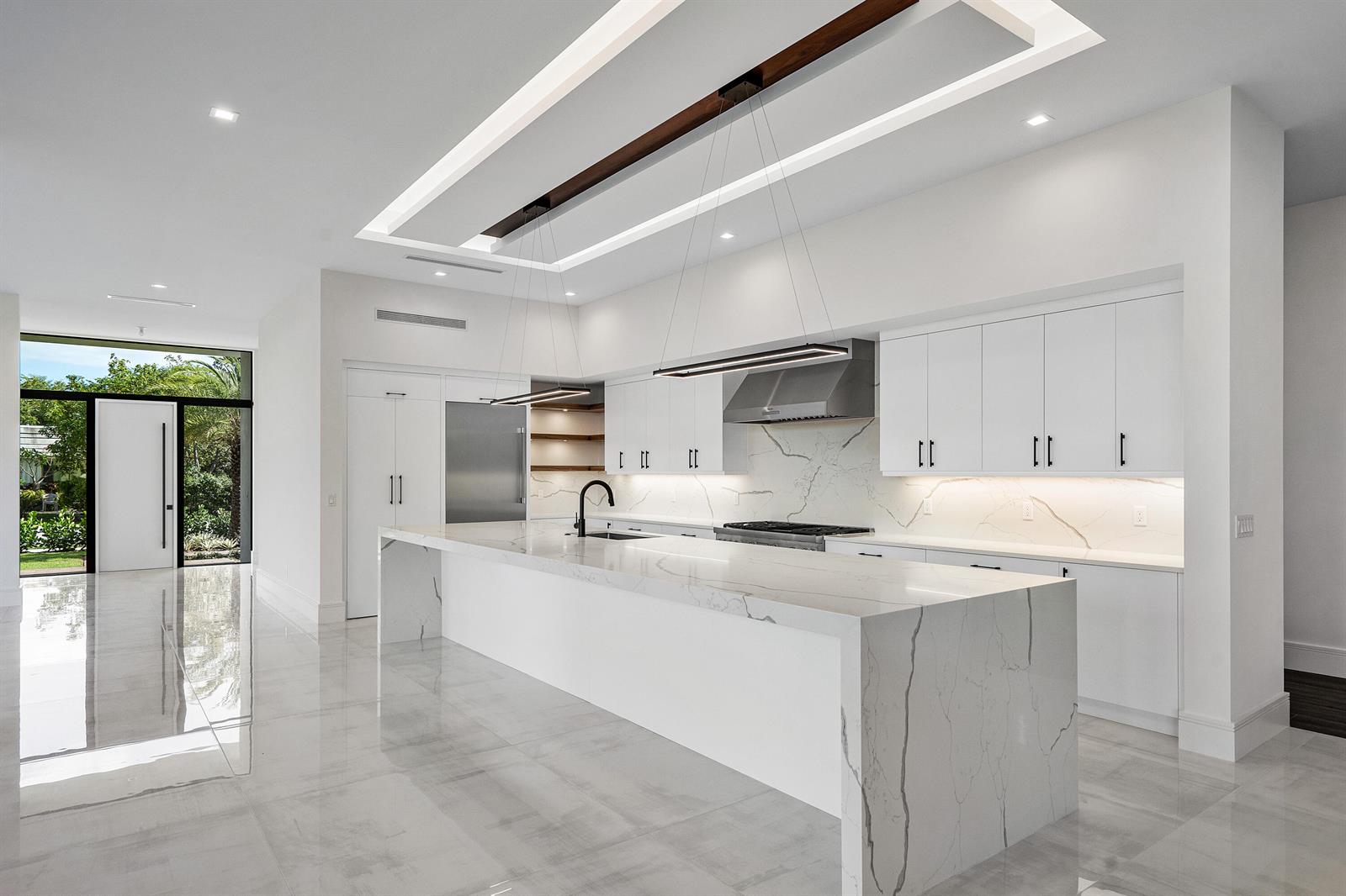 A modern white kitchen features a large marble waterfall island, stainless appliances, and recessed lighting — 10 Coconut Road, Delray Beach FL 33444, DELRAY BEACH, FL