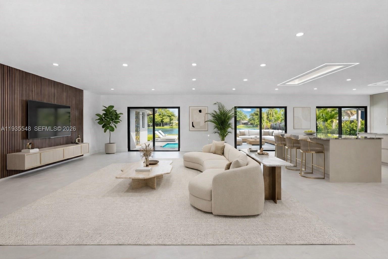 A modern, open-concept living room features a curved sofa, wood-slat wall, and large glass doors — 18735 NE 18th Ave, Miami FL 33179, MIAMI, FL