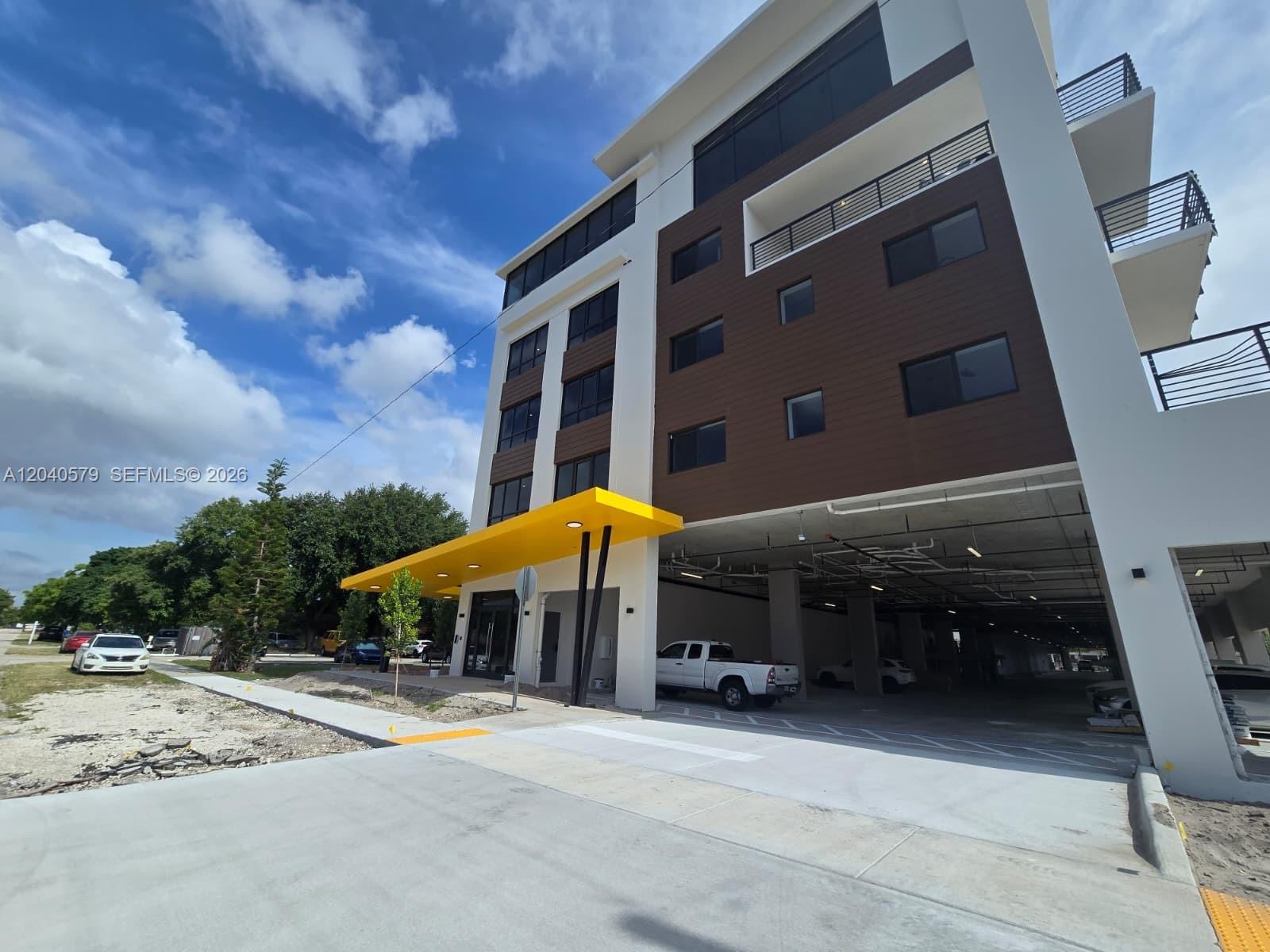 A modern multi-story building features a bright yellow entrance canopy and a ground-level parking garage — 2233 Fillmore St # 408, Hollywood FL 33020, HOLLYWOOD, FL