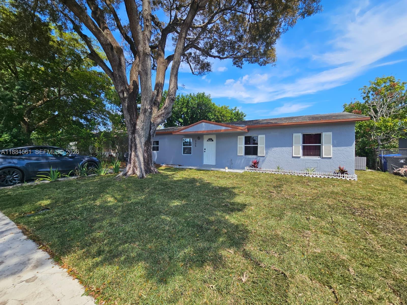 A single-story gray house with white shutters sits behind a large tree and lawn — 325 SW 80th Ter, North Lauderdale FL 33068, NORTH LAUDERDALE, FL