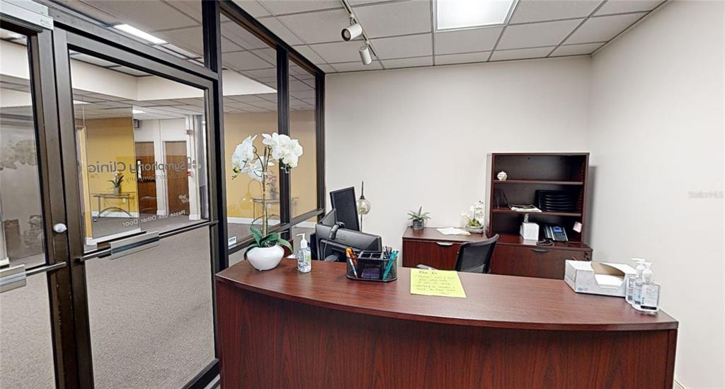 A reception area features a dark wood desk, glass-walled office partitions, and a white ceiling — 2815 NW 13TH STREET 2nd Floor, GAINESVILLE, FL