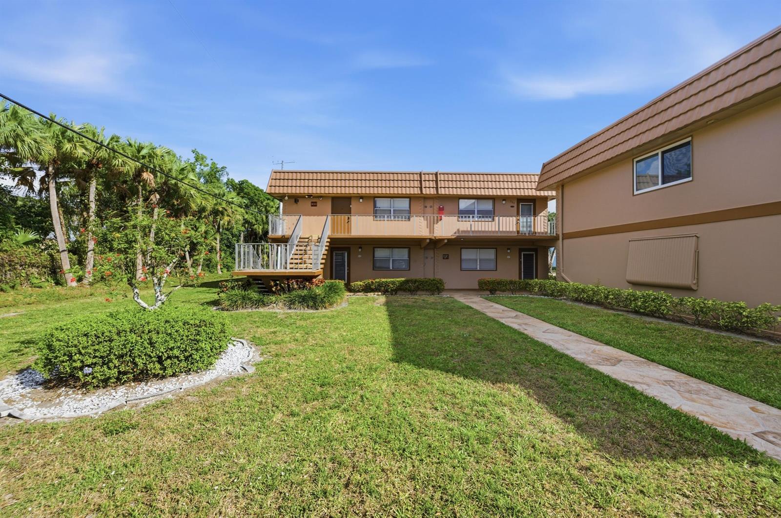 A two-story apartment building with a brown tiled roof, exterior stairs, and a grassy lawn — 336 Brittany G, Delray Beach FL 33446, DELRAY BEACH, FL