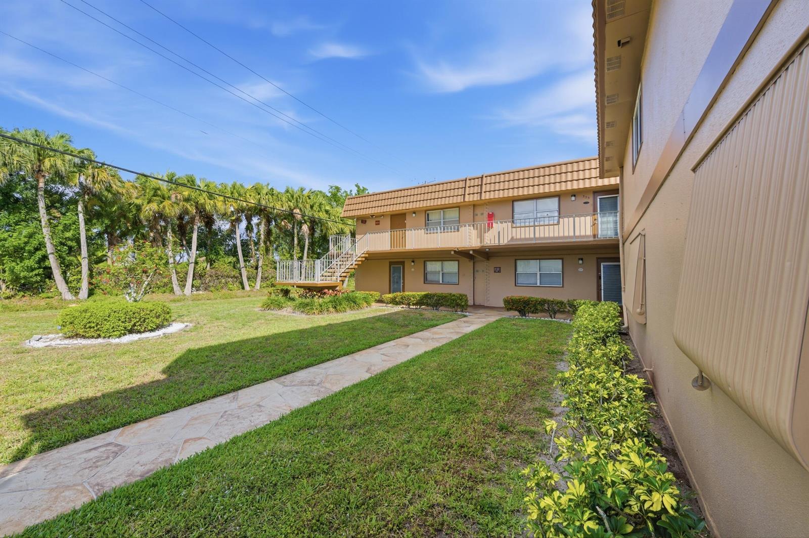 A two-story apartment building with a stone walkway, green lawn, and palm trees — 336 Brittany G, Delray Beach FL 33446, DELRAY BEACH, FL