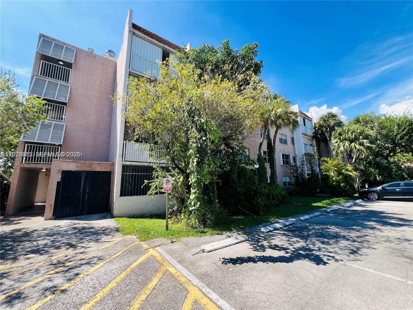 The exterior of a multi-story apartment building features pink stucco walls and a parking lot — 8405 NW 8th St # 304, Miami FL 33126, MIAMI, FL