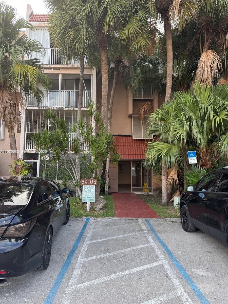 The exterior of a multi-story apartment building features palm trees, parking spaces, and a walkway — 8405 NW 8th St # 304, Miami FL 33126, MIAMI, FL